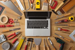 A laptop surrounded by assorted hand tools on a wooden surface.